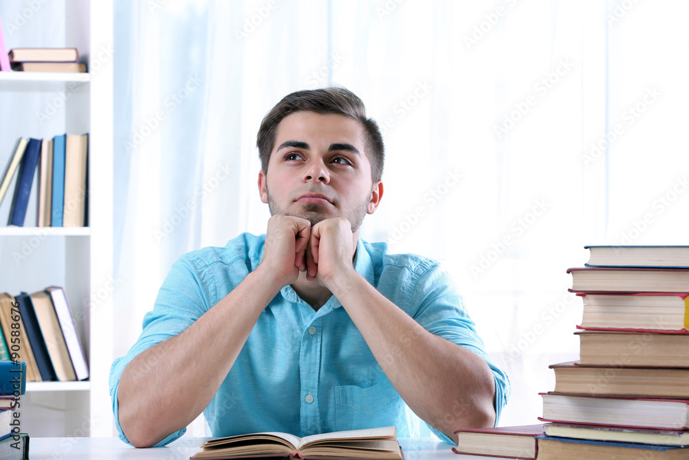 Young man reading book at table in room