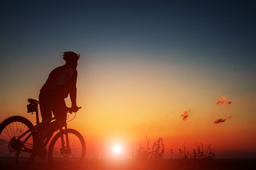 Wall Mural - Silhouette of a biker and bicycle on sky background.