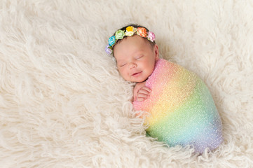 smiling newborn baby girl wearing a rainbow colored swaddle