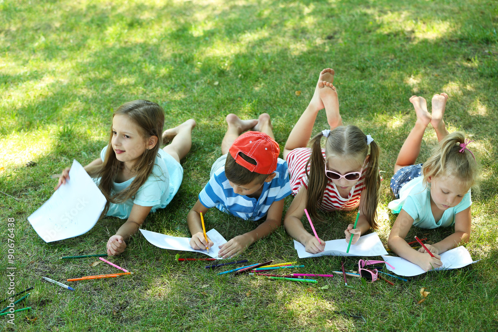 Happy active children lying on green grass and drawing in park