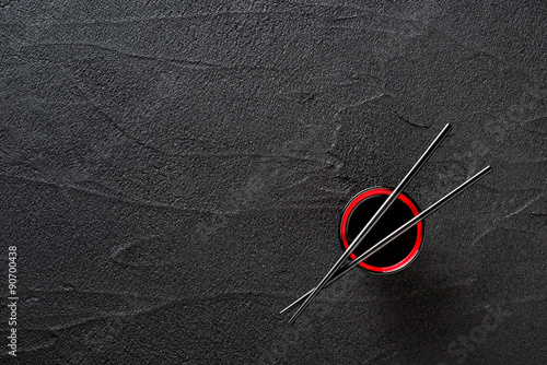 Chopsticks and bowl with soy sauce on black stone background Poster