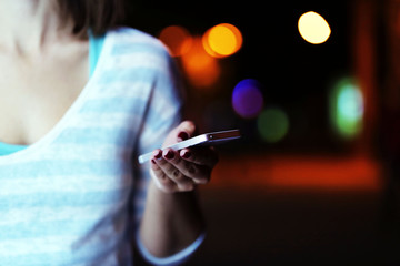 Poster - Female hand with mobile phone on blurred night lights background