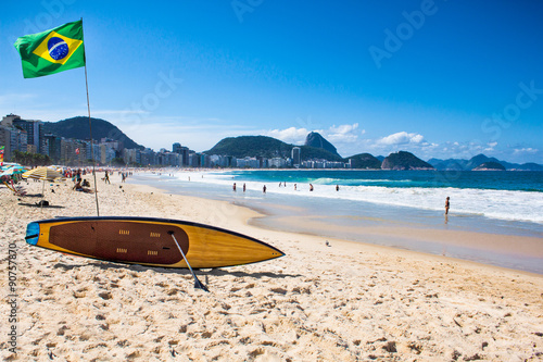 Fototapeta na szkło Flaga Brazylii i deska surfingowa na plaży Copacabana, Rio de Janeir