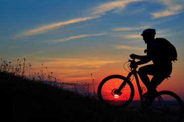 Wall Mural - Silhouette of a biker and bicycle on sky background.