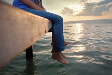 Low Section Of Two People Enjoing Sunset While Sitting On The Pier With Their Feet Above Water