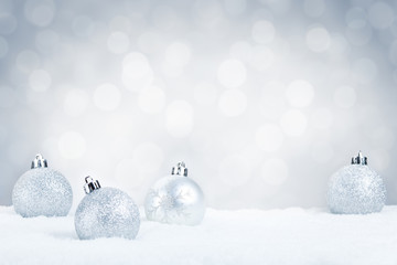 Silver Christmas baubles on snow with a silver background