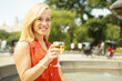 © DW labs Incorporated - A smiling young woman holds a  glass of wine as she stands by a park fountain.