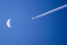 Airplane Flying Past The Moon Against Bright Blue