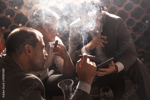 Trois hommes d'affaires assis dans la cave à vin de boire du vin et de la fumée de cigare, se reposer après une dure journée de travail Poster