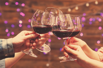 Clinking glasses of red wine in hands on bright lights background