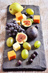  Cheese plate with grapes, figs, and pears on black slate board. Selective focus