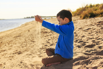 sand through his fingers. boy in warm clothing sitting on a beach and playing with sand