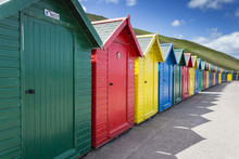 Row Of Colourful Beach Huts And Their Shadows With Green Hill Backdrop, West Cliff Beach, Whitby, North Yorkshire