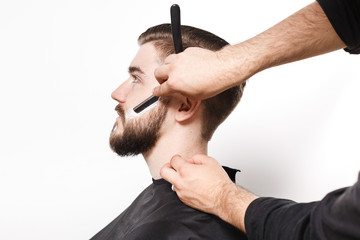 Hairdresser shaving young bearded man on white background