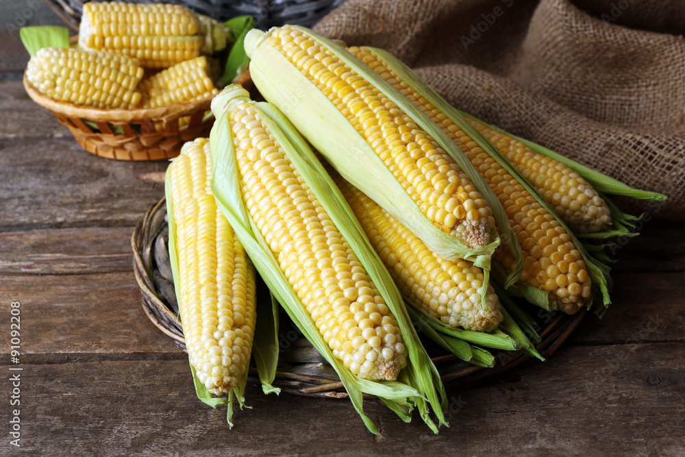 Fresh corn on cobs on wicker mat on wooden table, closeup