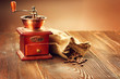 Coffee mill with burlap sack full of roasted coffee beans over wooden vintage table
