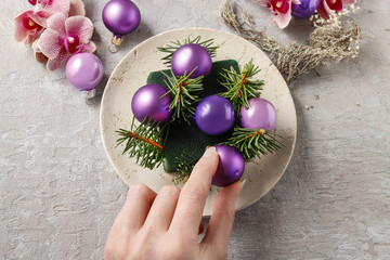 Woman making christmas decorations with violet balls, fir and or