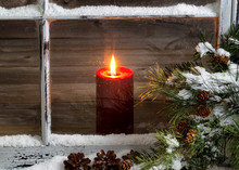 Christmas Red Candle With Snow Covered Home Window And Pine Tree