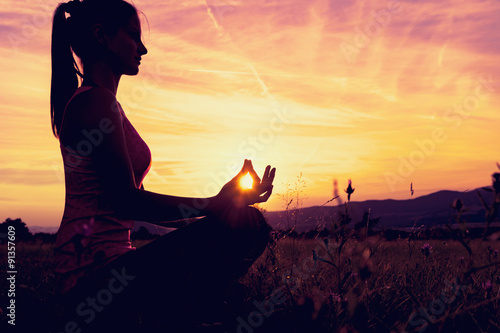 Fotografía Mujer atlética joven a practicar yoga en un prado en la puesta del sol, silueta