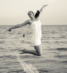 Happy brunette girl jumping over the sea. Stylized as retro photo filtered