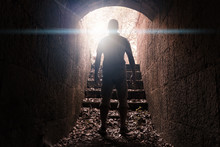 Man Stands In Dark Stone Tunnel With Glowing End