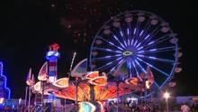 Fireworks Explode In The Night Sky Behind A Ferris Wheel At A Carnival Or State Fair.
