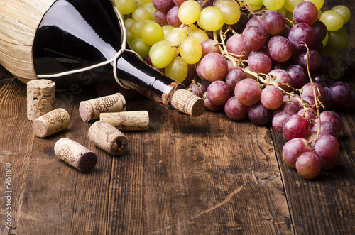 Naklejka ścienna fiasco di vino con uva e turaccioli su tavola di legno