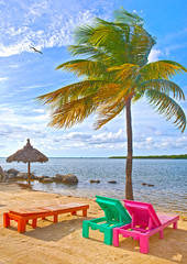 Colorful lounge chairs at a tropical paradise beach in Florida Keys. Beautiful aqua green waters of the ocean, hanging palm trees and a blue sky in the background