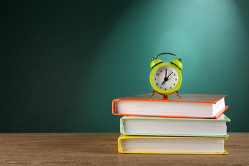 Poster - Stack of books with alarm clock on desk on green chalkboard background