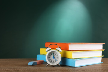 Poster - Stack of books with alarm clock and eraser on green chalkboard background