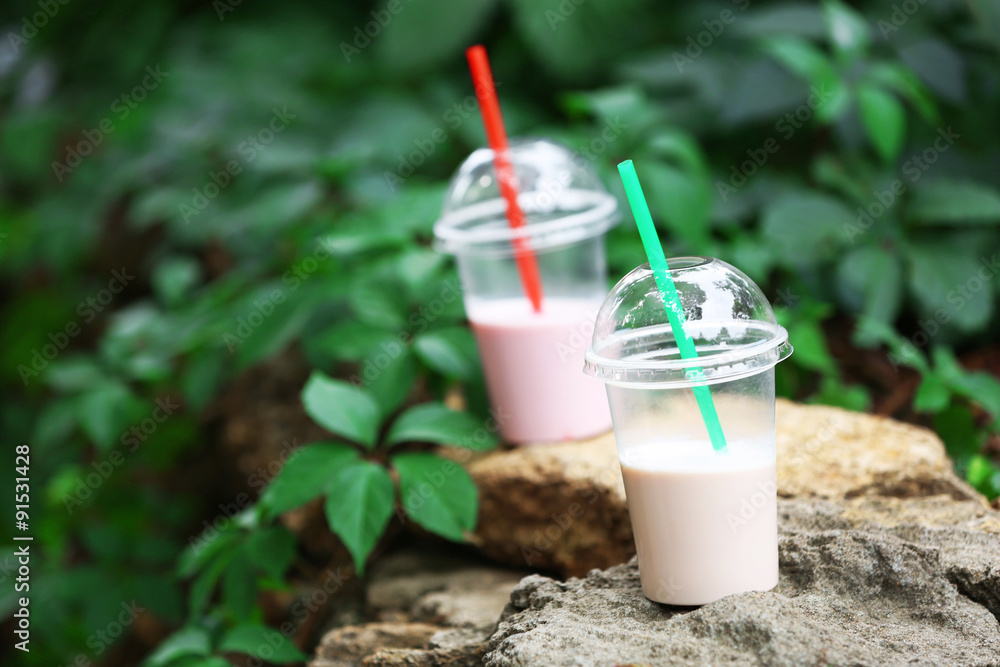 Plastic cups of milkshake on green background, outdoors