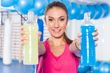 Young girl with two isotonic drink (yellow, blue), gym. She is ready for workout.