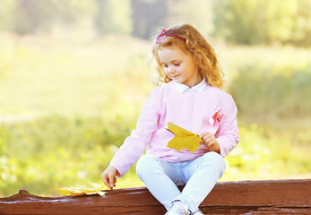 Cute little girl child with yellow maple leafs in autumn day