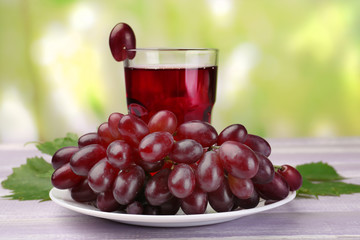 Wall Mural - Glass of grape juice on wooden table on light blurred background