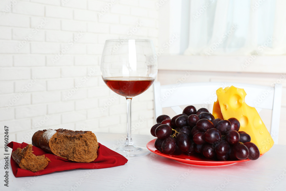 Glass of wine with bread and grapes on table in kitchen