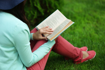 Wall Mural - Young woman with book sitting on green grass outdoors