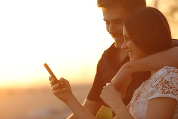 Wall Mural - Couple using a smartphone in a sunset back light