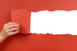 Hand tearing red paper background strip banner hole open opening revealing white space for copy text inside torn paper photo