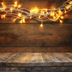 wood board table in front of Christmas warm gold garland lights on wooden rustic background. filtered image. selective focus
