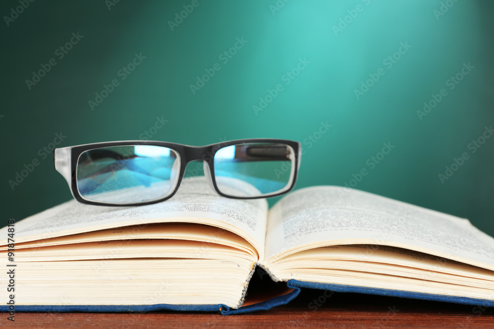 Open book with glasses on desk on green chalkboard background