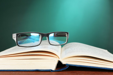 Canvas Print - Open book with glasses on desk on green chalkboard background