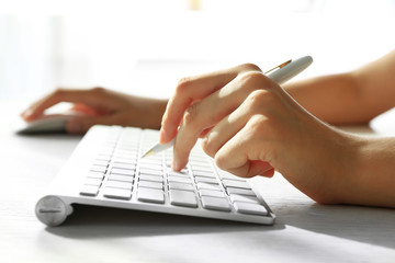 Wall Mural - Female hand with pen typing on keyboard at table, closeup