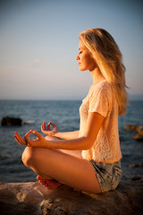 Beautiful young blond woman meditating on a beach at sunrise in