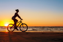 Silhouette Of Sporty Woman Riding Bicycle On Multicolored Sunset
