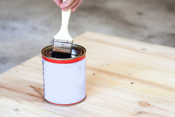 Carpenter is soaking his brush into the can of paint.