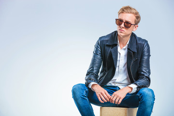 skinny man wearing sun glasses and leather jacket while sitting