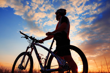 Wall Mural - Silhouette of a biker and bicycle on sunset background.