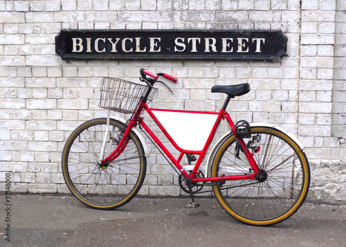 Fototapeta Bicycle Street sign with a bicycle leaning against a wall with an empty panel for your logo or message