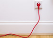 Das Foto zeigt ein rotes Stromkabel in einer Steckdose