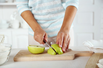 Poster - Female hands slicing apple for pie, close-up, on light background